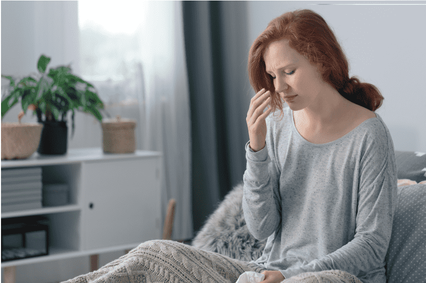 Woman with headache sitting on couch with blanket.