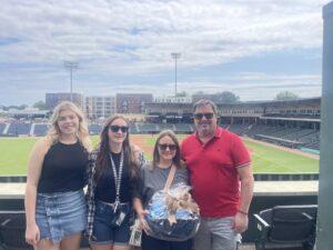 family standing at Greenville Drive field with a gift basket from Waldrop.