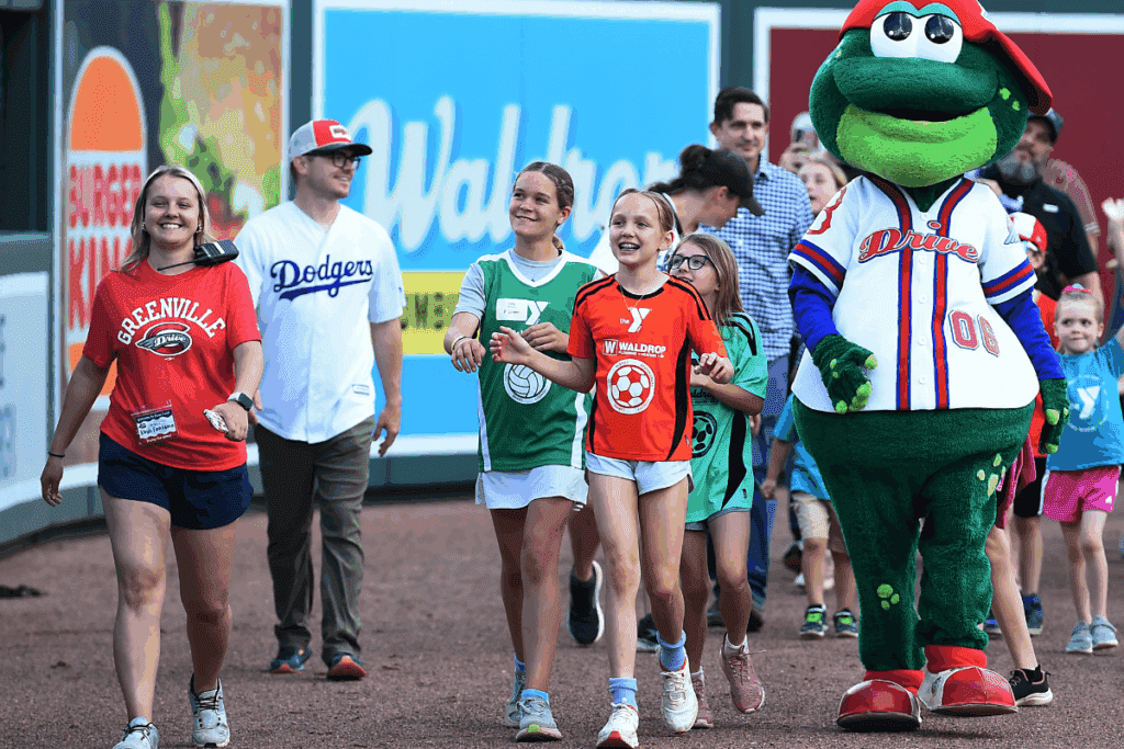 Kids walking on Greenville Drive field with Reedy Rippit for Waldrop's Youth and Sports Night.