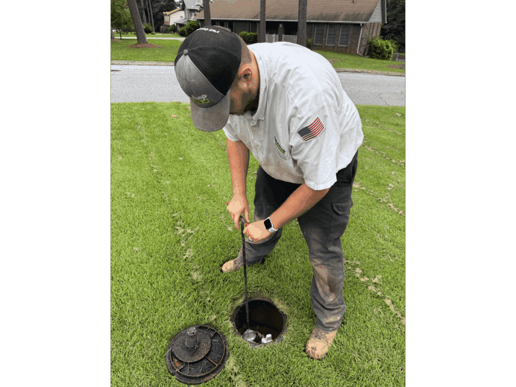 plumber at water meter shutoff in a yard.