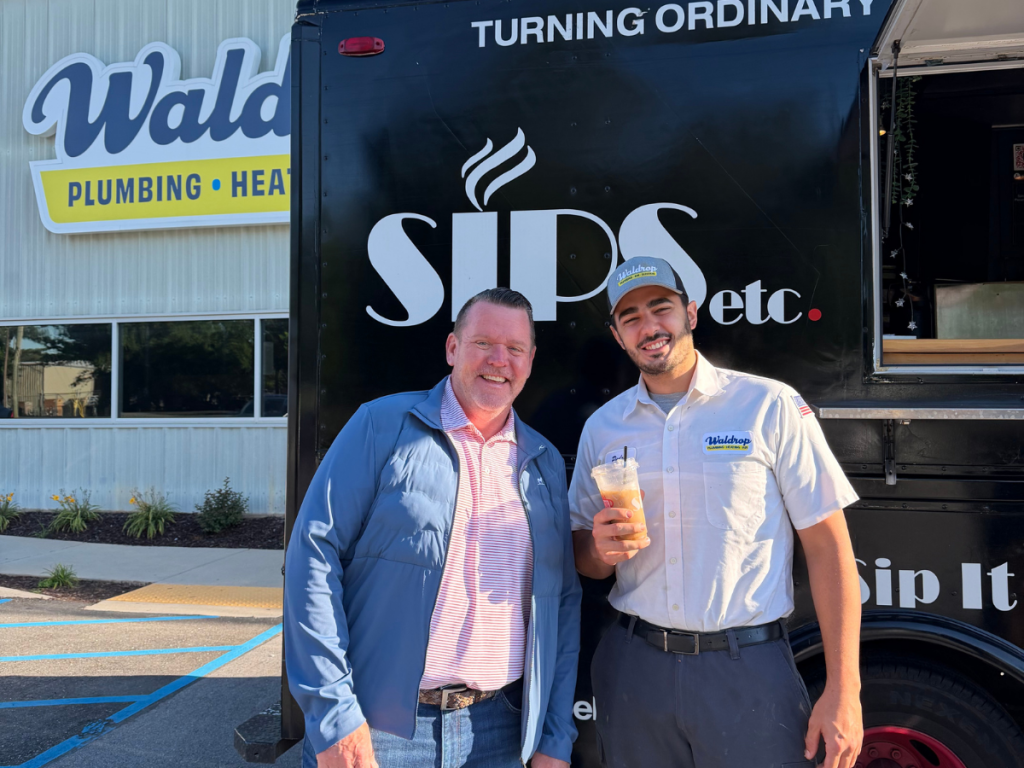 Two men smiling in front of a black SIPS truck; one in a blue jacket, the other in a Waldrip uniform holding a cold drink.
