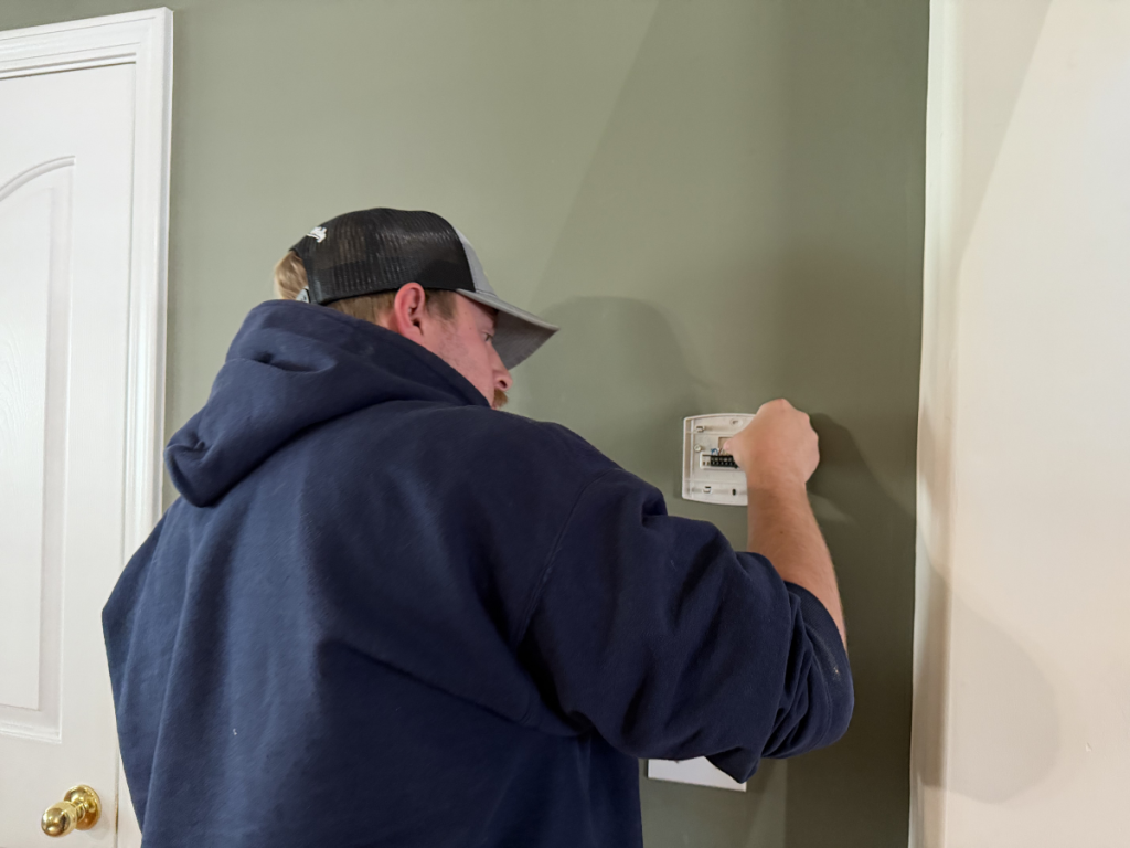 Worker in a navy hoodie and cap installs a wall plate with wiring on a green wall