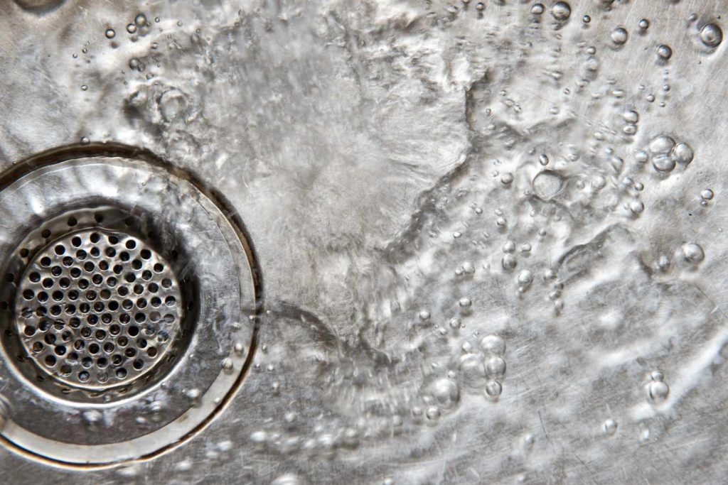 Close-up of a stainless steel sink drain with a perforated strainer and bubbles on the surface.