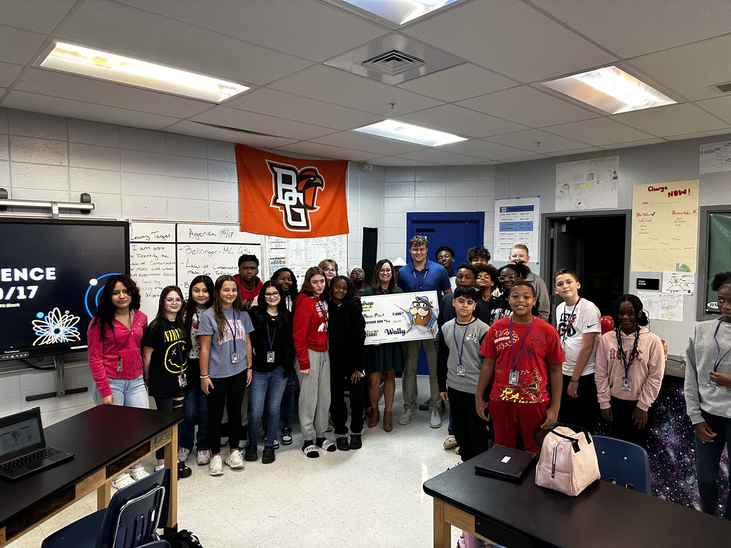 Group of students in a classroom posing with a large ceremonial check on display.