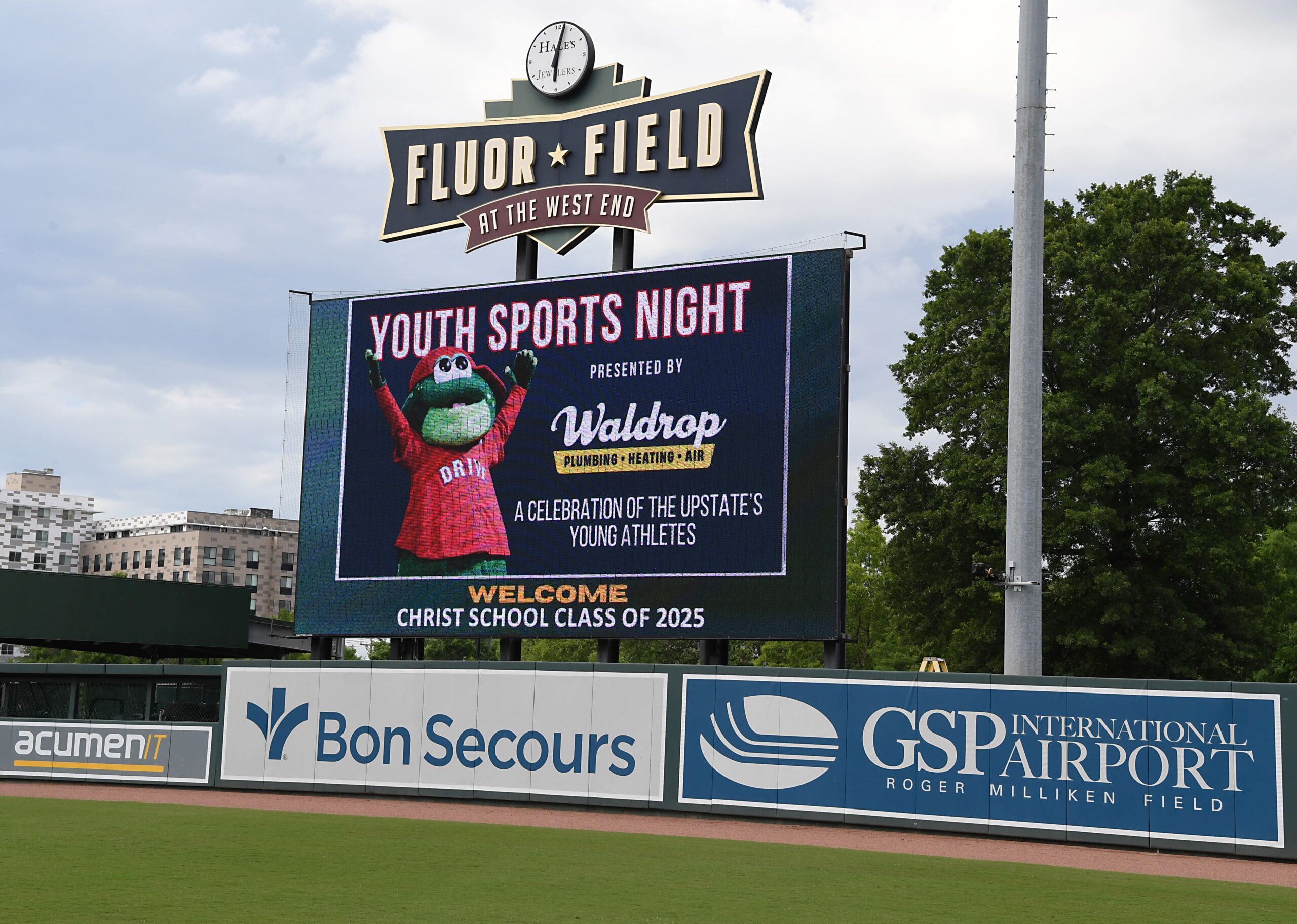 Fluor Field sign above a large LED scoreboard advertising "Youth Sports Night" with a green frog mascot on the screen against a blue background.