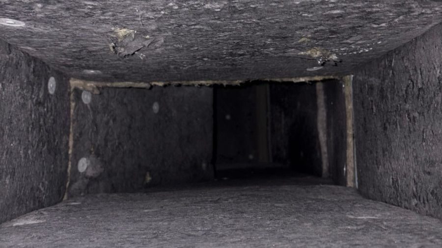 Dark, narrow concrete duct interior receding into darkness with rough, dusty walls and ceiling.