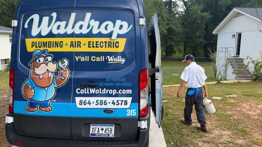 Blue Waldrop Plumbing van with cartoon mascot on rear: 'Plumbing · Air · Electric', phone number, and 'Y'all Call Wally'; a technician walks away carrying a white gas can toward a house.